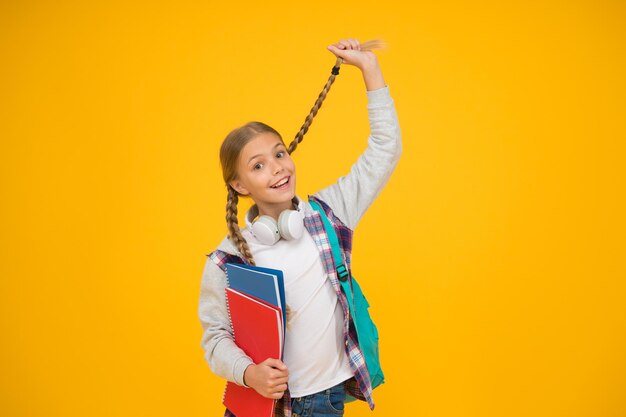 Capelli facili per il ritorno a scuola. Il piccolo bambino carino indossa uno stile di capelli lunghi. Adorabile piccola ragazza tenere treccia di capelli su sfondo giallo. Treccia di capelli per la scuola. Salone di bellezza.