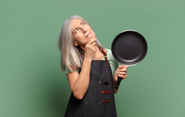 capelli grigi bella donna chef di mezza età con una padella