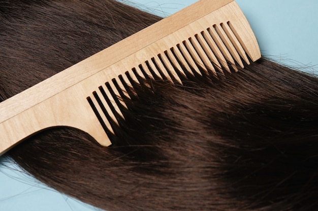 Capelli lunghi castani e spazzola per capelli in legno naturale su sfondo blu