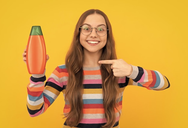 Capelli lunghi ragazza teenager allegra in vetri che puntano il dito sulla promozione della bottiglia di lozione per la pelle