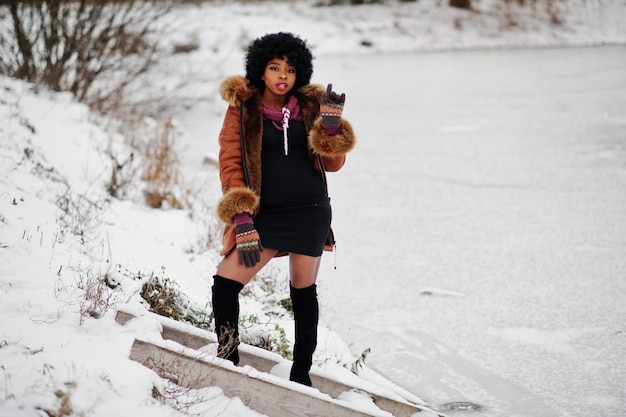 Capelli ricci donna afroamericana indossare su cappotto di pelle di pecora e guanti poste al giorno d'inverno contro il lago ghiacciato