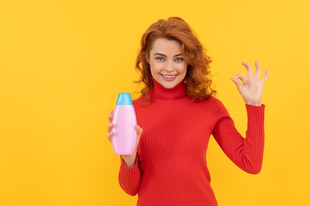 Capelli tinti ricci ragazza rossa felice che presenta il prodotto per la cura del corpo di shampoo mostra gesto ok, cura dei capelli.