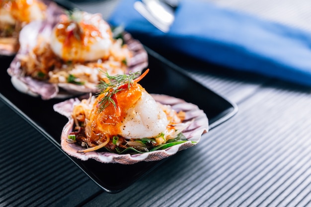 Capesante alla griglia in guscio con insalata di pomelo piccante servita in piastra nera.