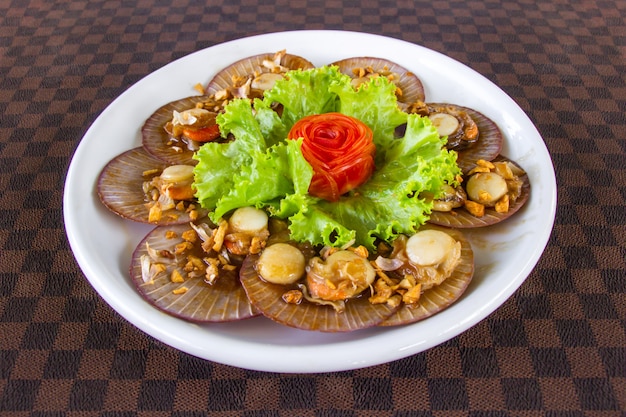 Capesante fritte con aglio decorato con carote su un piatto di ceramica bianco messo sul pavimento in pelle.