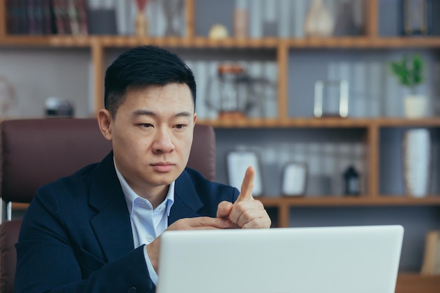 Capo d'affari asiatico che parla con i colleghi in videochiamata guardando lo schermo del laptop che lavora nella riunione online dell'ufficio