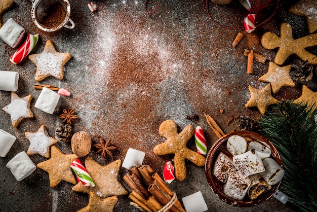 Capodanno, prelibatezze natalizie. Tazza di cioccolata calda con marshmallow fritto, biscotti con stelle allo zenzero, pan di zenzero, caramelle a strisce, spezie cannella, anice, cacao, zucchero a velo. Cornice vista dall'alto