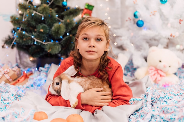 Capodanno una ragazza con un maglione di Capodanno tiene un coniglio vicino all'albero di Natale