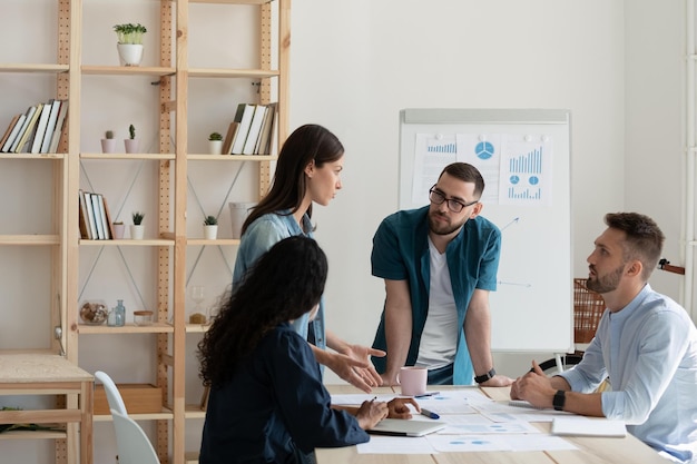 Capogruppo maschile concentrato con gli occhiali in piedi vicino al tavolo che ascolta lo specialista di marketing fmale durante la riunione di brainstorming in ufficio Dipendenti impegnati motivati che lavorano sulla strategia di sviluppo del progetto