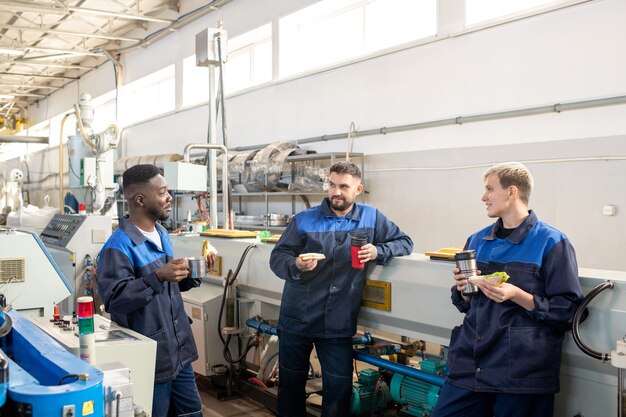 Caposquadra soddisfatto con gli occhiali che guarda il rapporto di produzione con gli ingegneri mentre pianifica ulteriori lavori insieme