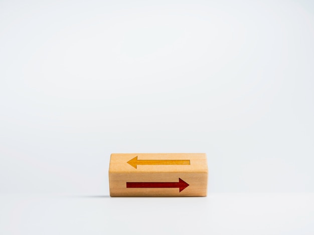 Capovolgimento del blocco di legno con due diverse icone di frecce che si muovono in modo opposto su sfondo bianco. La scelta del percorso corretto tra sinistra, destra. Concetto di decisione.
