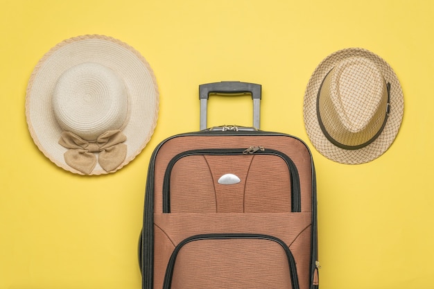 Cappelli da uomo e da donna e una valigia da viaggio su sfondo giallo. Disposizione piatta.