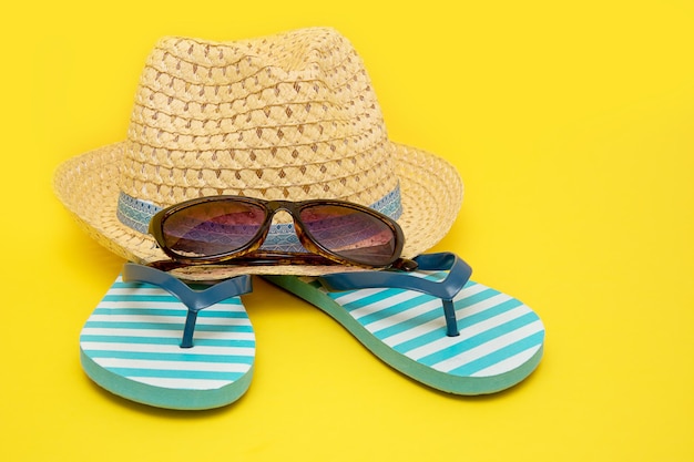 Cappello con occhiali da sole e infradito a righe su sfondo giallo