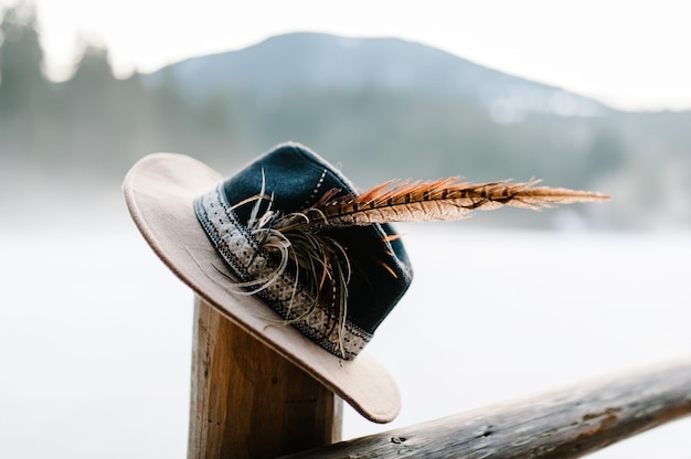 Cappello con piume realizzato a mano su staccionata in legno, colonna in inverno sulla superficie delle montagne