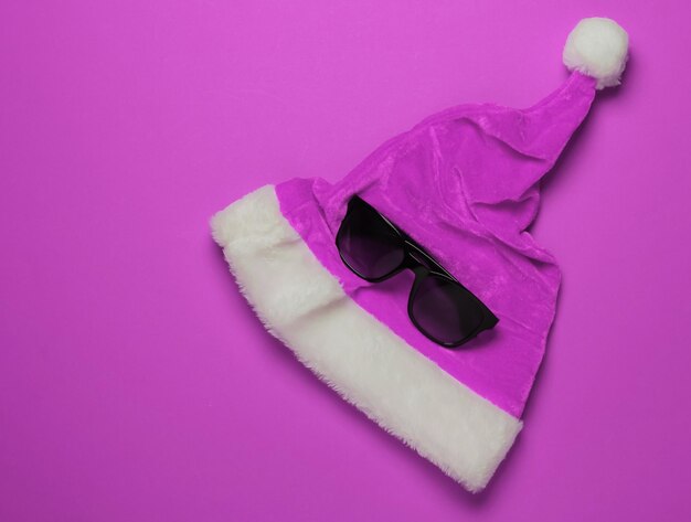 Cappello da Babbo Natale e occhiali da sole su sfondo rosa. Capodanno, vacanze di Natale in luoghi caldi e soleggiati. Vacanza al mare. Concetto di viaggio