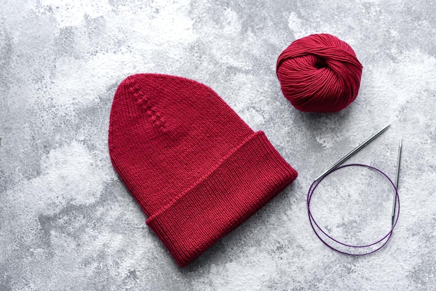 Cappello da donna rosso caldo lavorato a maglia su sfondo di cemento Hobby e tempo libero