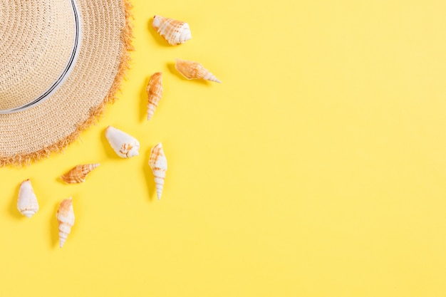 Cappello da spiaggia con conchiglie sul tavolo giallo marrone.