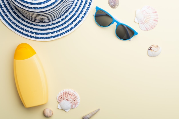 Cappello da spiaggia, occhiali da sole e crema solare sono tra le conchiglie su una superficie beige