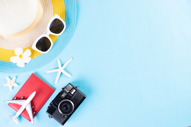 Cappello da spiaggia, occhiali da sole, macchina fotografica, passaporto e infradito su sfondo azzurro. Estate o vacanze.