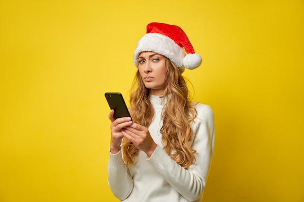 Cappello della Santa di Natale della donna su colore giallo con lo smartphone in mano