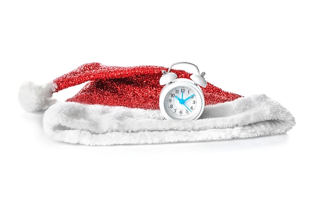 Cappello di Babbo Natale e piccolo orologio su sfondo bianco. Concetto di conto alla rovescia di Natale