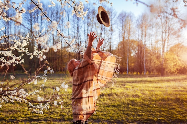 Cappello di lancio della donna felice nel giardino di primavera. Donna che si diverte.