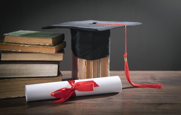 Cappello di laurea, libro e diploma sul tavolo di legno.