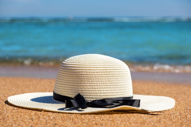 Cappello di paglia della donna bianca che pone sulla spiaggia di sabbia tropicale con acqua dell'oceano vibrante blu nella priorità bassa il giorno di estate soleggiato. Vacanze e concetto di viaggio di destinazione.