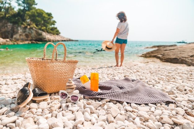 Cappello di paglia e borsa da spiaggia con pinne e crema solare in spiaggia donna sullo sfondo