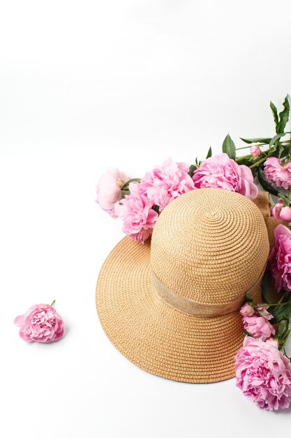 cappello di paglia intrecciata, fiori di peonia rosa su bianco, vista dall'alto