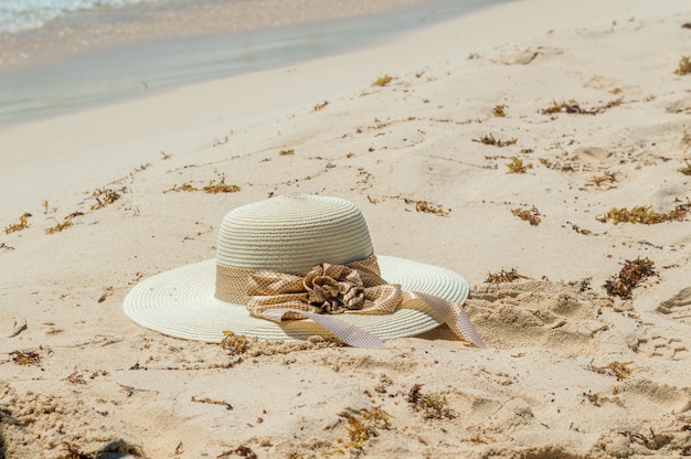 Cappello di paglia nella sabbia, concetto di protezione solare. Vita con cappello e toni foglia di palma, vacanze al mare nelle isole. Cappello con nastro sulla spiaggia.