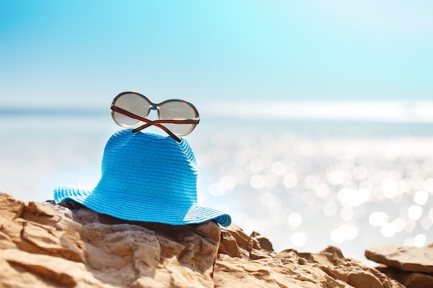Cappello e occhiali da sole sulla roccia, mare limpido. Concetto di vacanza di viaggio.