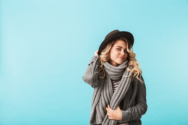 Cappello e sciarpa da portare della donna bionda abbastanza giovane isolati sopra la parete blu