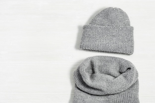 Cappello e sciarpa grigi tricottati su fondo di legno bianco. Vestiti caldi alla moda per ragazza o donna. Disteso. Vista dall'alto. Copia spazio.