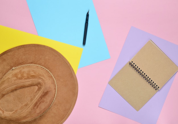 Cappello in feltro, quaderno, penna sul muro di carta colorata. Il concetto di viaggio. Minimalismo, vista dall'alto