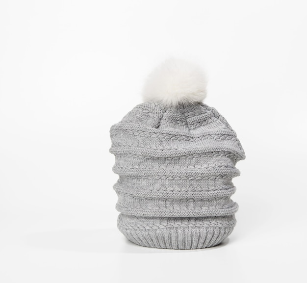 Cappello lavorato a maglia grigio con pompon su superficie bianca, abbigliamento caldo e comodo