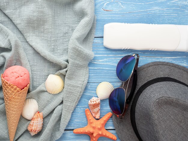 Cappello, occhiali da sole e conchiglie giacciono su un tavolo di legno blu