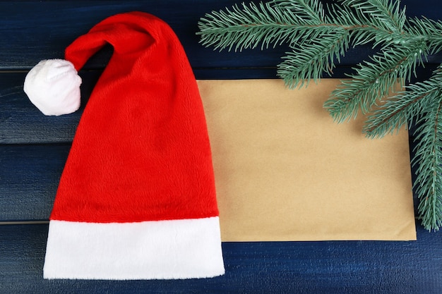 Cappello rosso di Babbo Natale con ramo di abete e foglio di carta su fondo in legno colorato