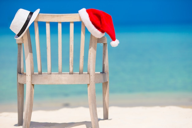 Cappello rosso di Santa e cappello di paglia bianco sulla sedia di spiaggia alla vacanza tropicale