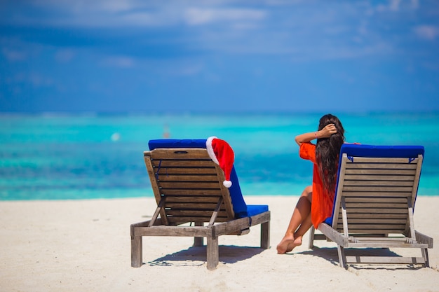 Cappello rosso di Santa sulla sedia longue alla spiaggia bianca tropicale