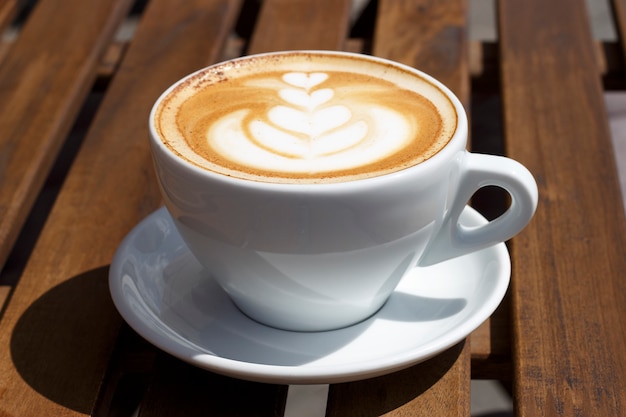 Cappuccino caldo con schiuma e modello su fondo di legno, vista laterale