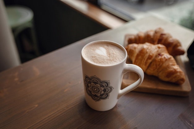 Cappuccino con bella arte del latte e croissant su fondo di legno sul tavolo. Colazione perfetta al mattino. Stile rustico.