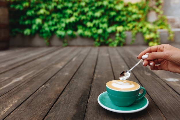 Cappuccino di arte del latte del caffè fresco caldo in una bella tazza color turchese sul piattino