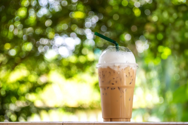 Cappuccino di ghiaccio in tazza plastice. Take away package. Bevanda con il backgr del bokeh verde della natura