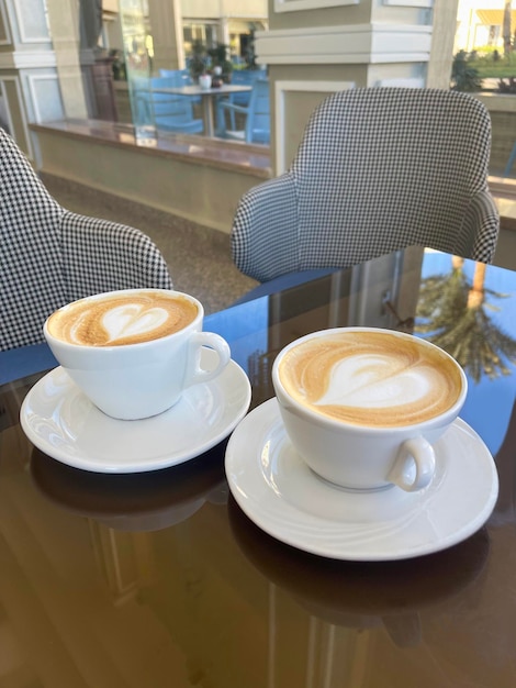 Cappuccino in due tazze bianche decorate con cuori in cima su un tavolo di vetro