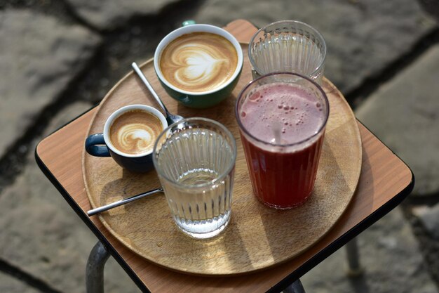 Cappuccino macchiato limonata al lampone e due bicchieri d'acqua su un vassoio di legno su un tavolo in un parco pubblico