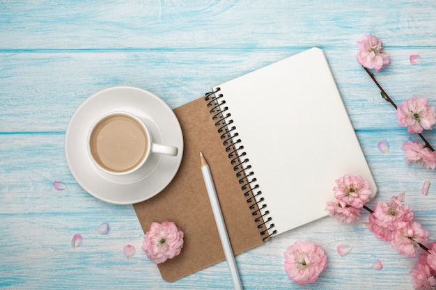 Cappuccino tazza bianca con fiori di sakura, notebook su un tavolo di legno blu