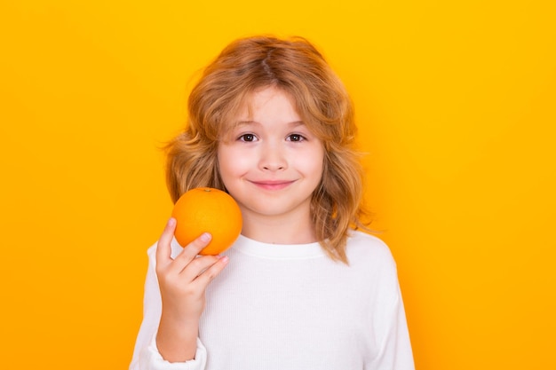 Capretto con arancia in studio Studio ritratto di bambino carino tenere arancione isolato su sfondo giallo