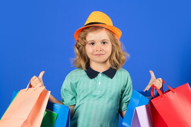 Capretto con molte borse della spesa in studio Ragazzino divertente in abbigliamento estivo per bambini con borse della spesa su sfondo isolato