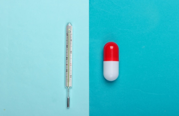 Capsula della pillola e termometro su sfondo blu. Vista dall'alto. Minimalismo