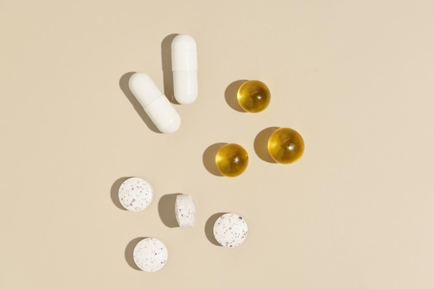 Capsule bianche e gialle su sfondo beige isolato con un bicchiere d'acqua Concetto di farmacia assunzione giornaliera di pillole vitamine per migliorare la salute e la bellezza